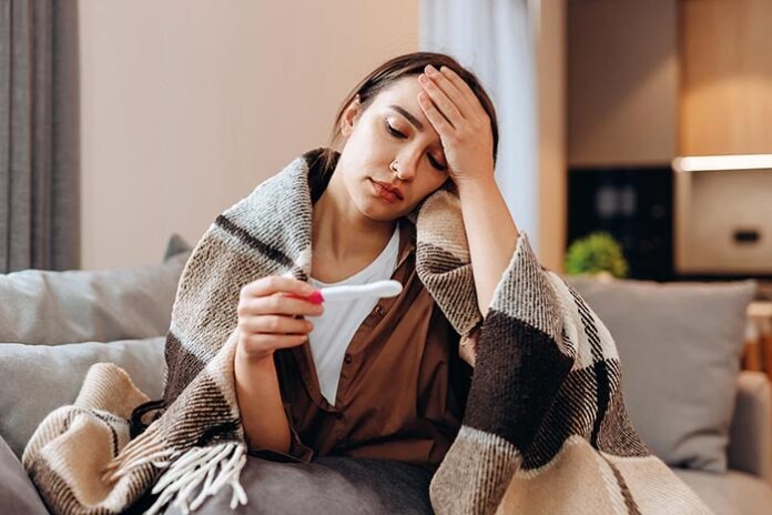 Sick sad girl sitting on the sofa covered with a blanket. He loo
