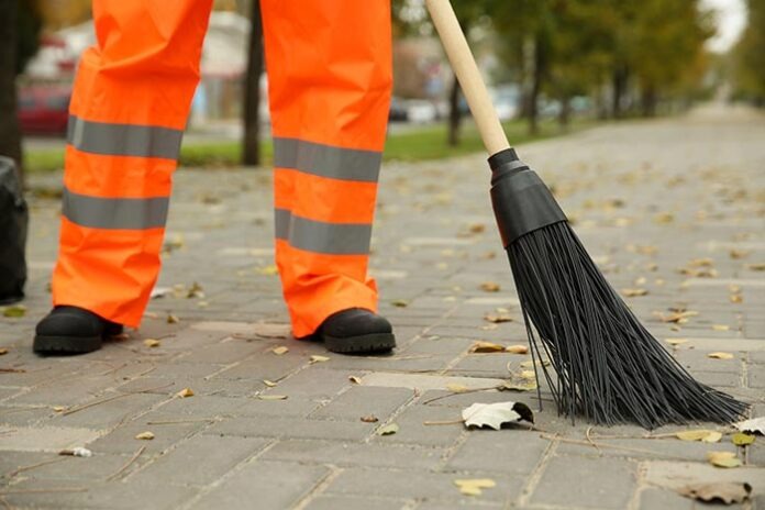Street cleaner sweeping fallen leaves outdoors on autumn day, cl