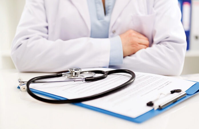 Female doctor sitting at desk with stethoscope and medical form