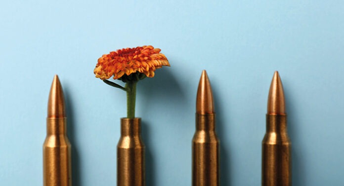 Bullets and cartridge case with beautiful flower on light blue b