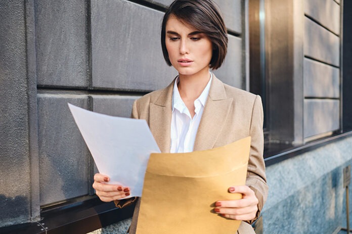 Young serious businesswoman in suit thoughtfully working with pa