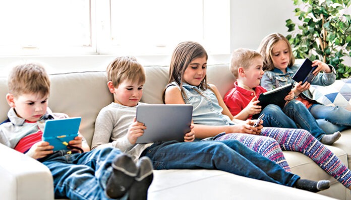 group child Sitting On Sofa At Home With tablet and video game