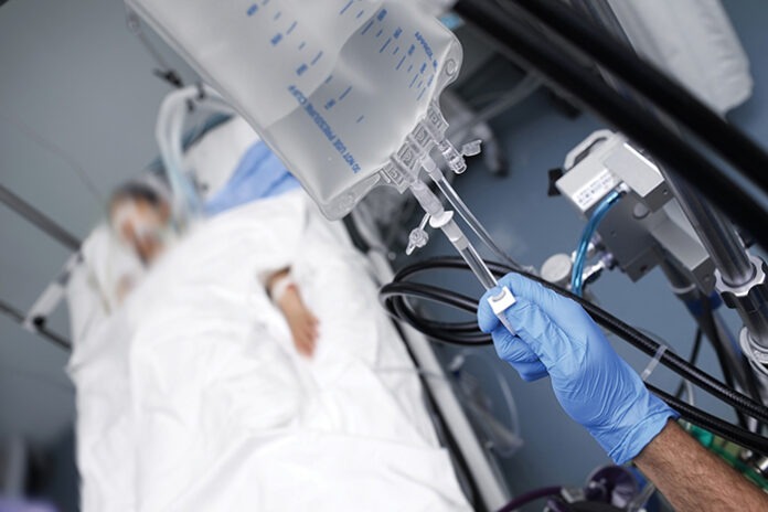 Male person with gloved hand turns off the intravenous drug syst