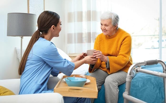 Care worker serving dinner for elderly woman in geriatric hospic