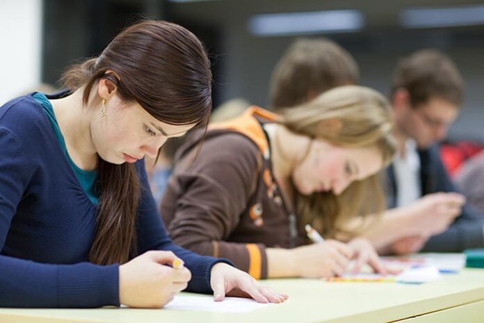 pretty female college student sitting in a classroom full of stu